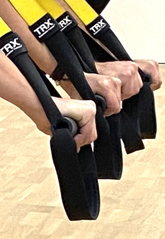 Hände halten die gelb-schwarzen TRX-Schlingen während eines Suspension Gruppenkurs Trainings im Fitorama Basel.