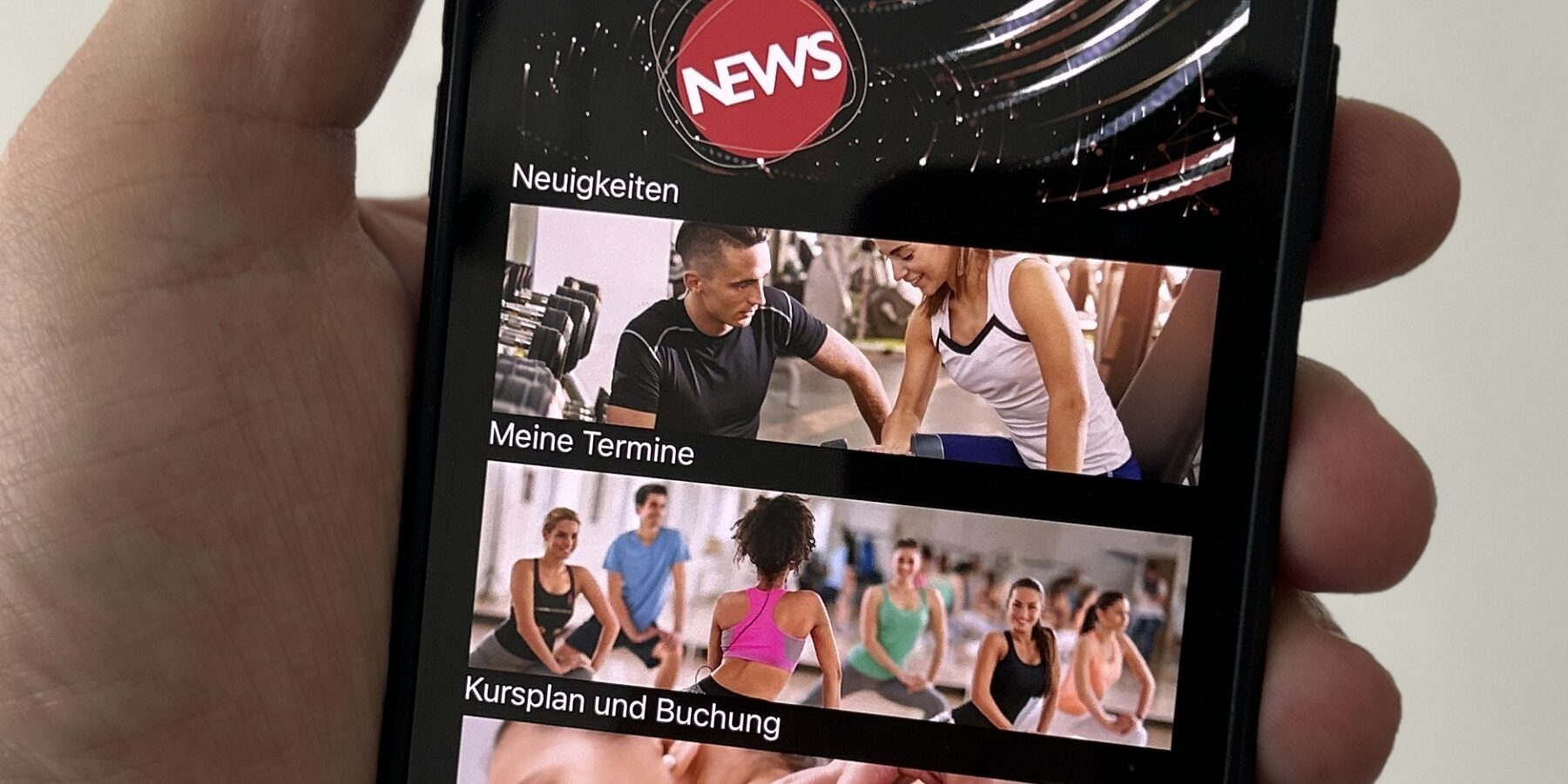 Eine Hand hält ein Smartphone, das die Startseite der Fitorama Clubconnector App anzeigt, mit Optionen für Neuigkeiten, Termine, Kursbuchung und Training.