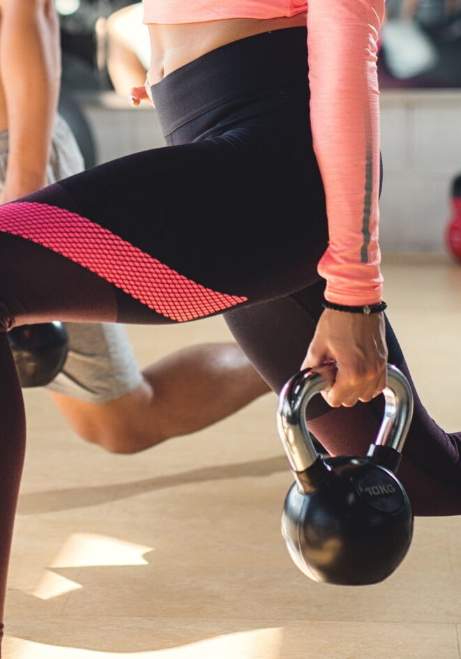 Detail einer Kursteilnehmerin im Ausfallschritt mit Kettlebells im Gruppenkurs Beachbody Fit.