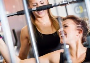 Lachende Kundin beim Latzug-Training im Fitorama Basel, professionell unterstützt durch eine Trainerin.