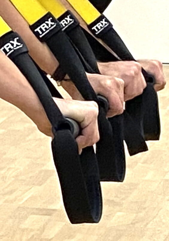 Hände halten die gelb-schwarzen TRX-Schlingen während eines Suspension Gruppenkurs Trainings im Fitorama Basel.